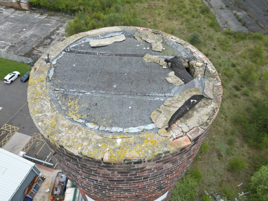 Close-range drone image of a failing chimney stack capping with displaced copings