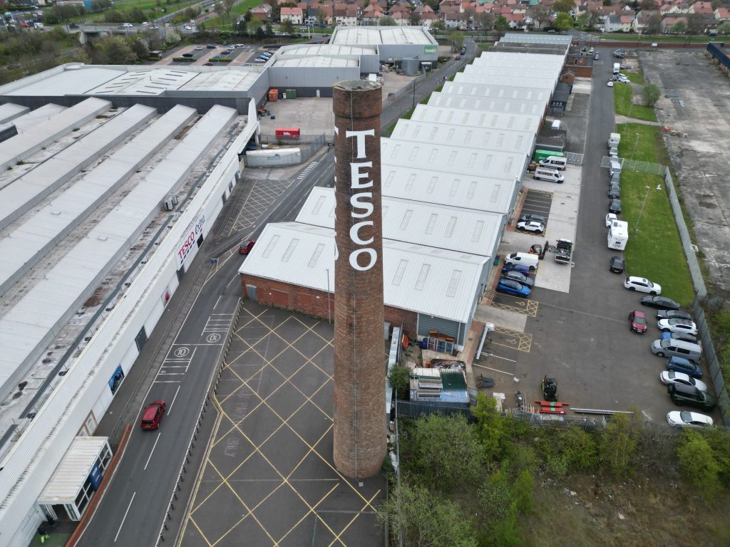 Brick chimney stack above a live retail service yard, inspected by drone