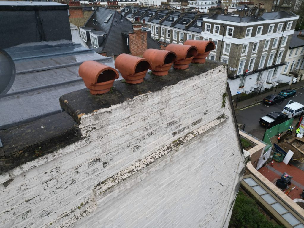 Close-range drone image of a party wall, chimney pots and weathered capping